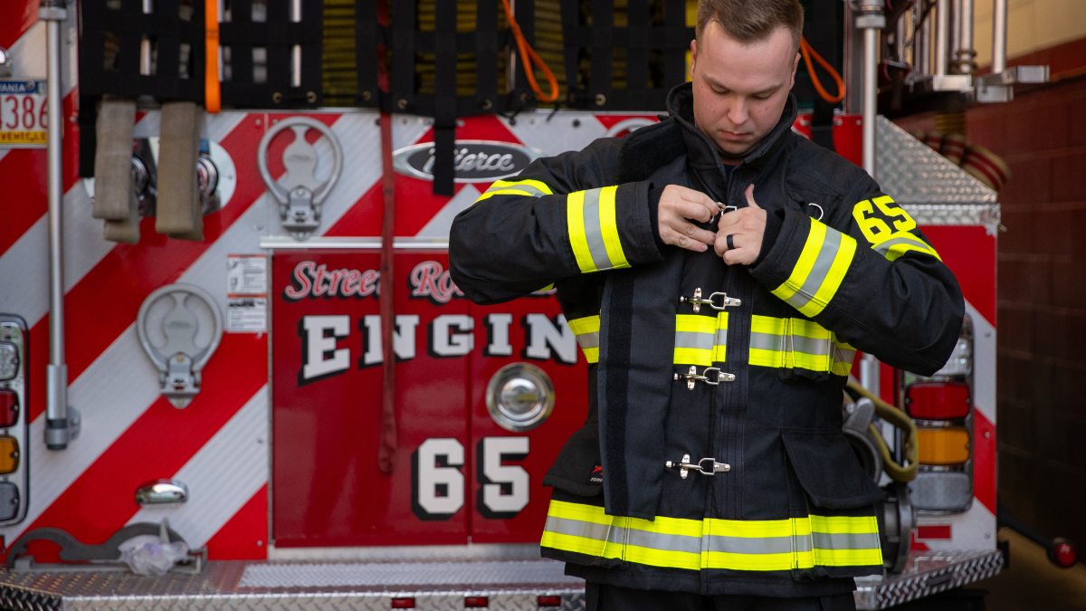 Firefighter adjusting properly fitted structural turnout gear before responding to an incident, highlighting the importance of PPE fit for comfort, mobility, and protection.