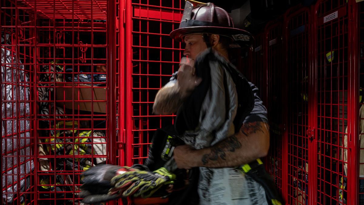 Firefighter donning non-PFAS structural turnout gear inside a fire station before training or response.