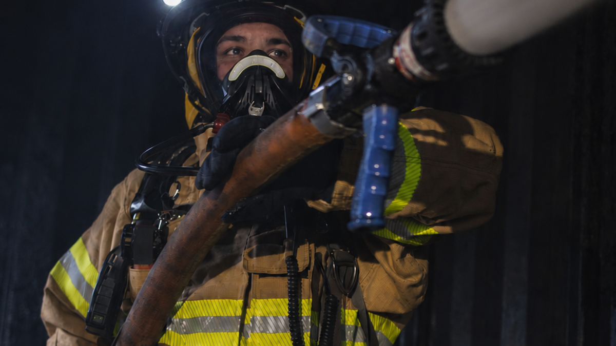 Firefighter wearing non-PFAS structural turnout gear operating a charged hoseline during live fire training.